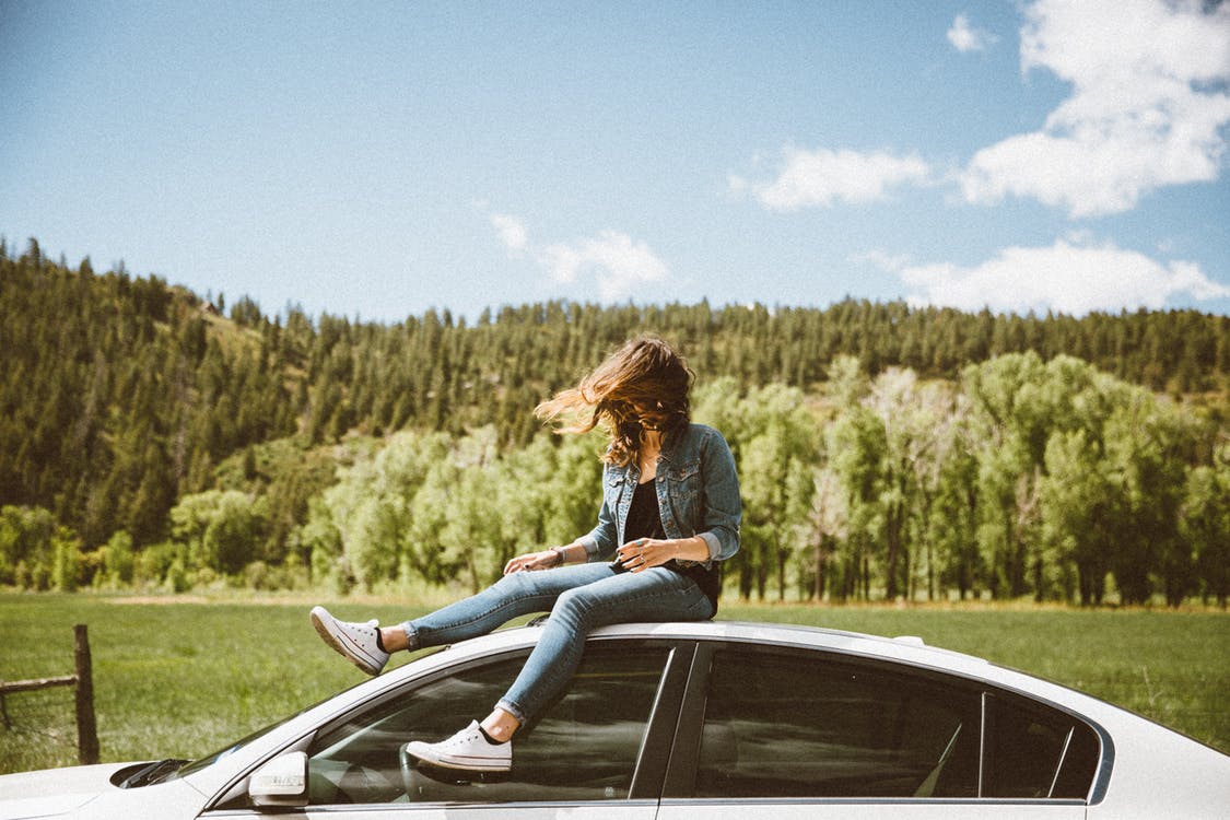 A female relaxing outside of a car. Photo by: Pexels.com