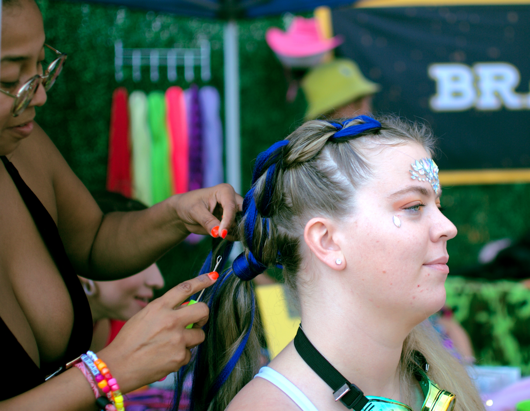 Festival goer gets her hair braided with multicolored hair extensions in the VIP area. Photo by Marissa Novel.